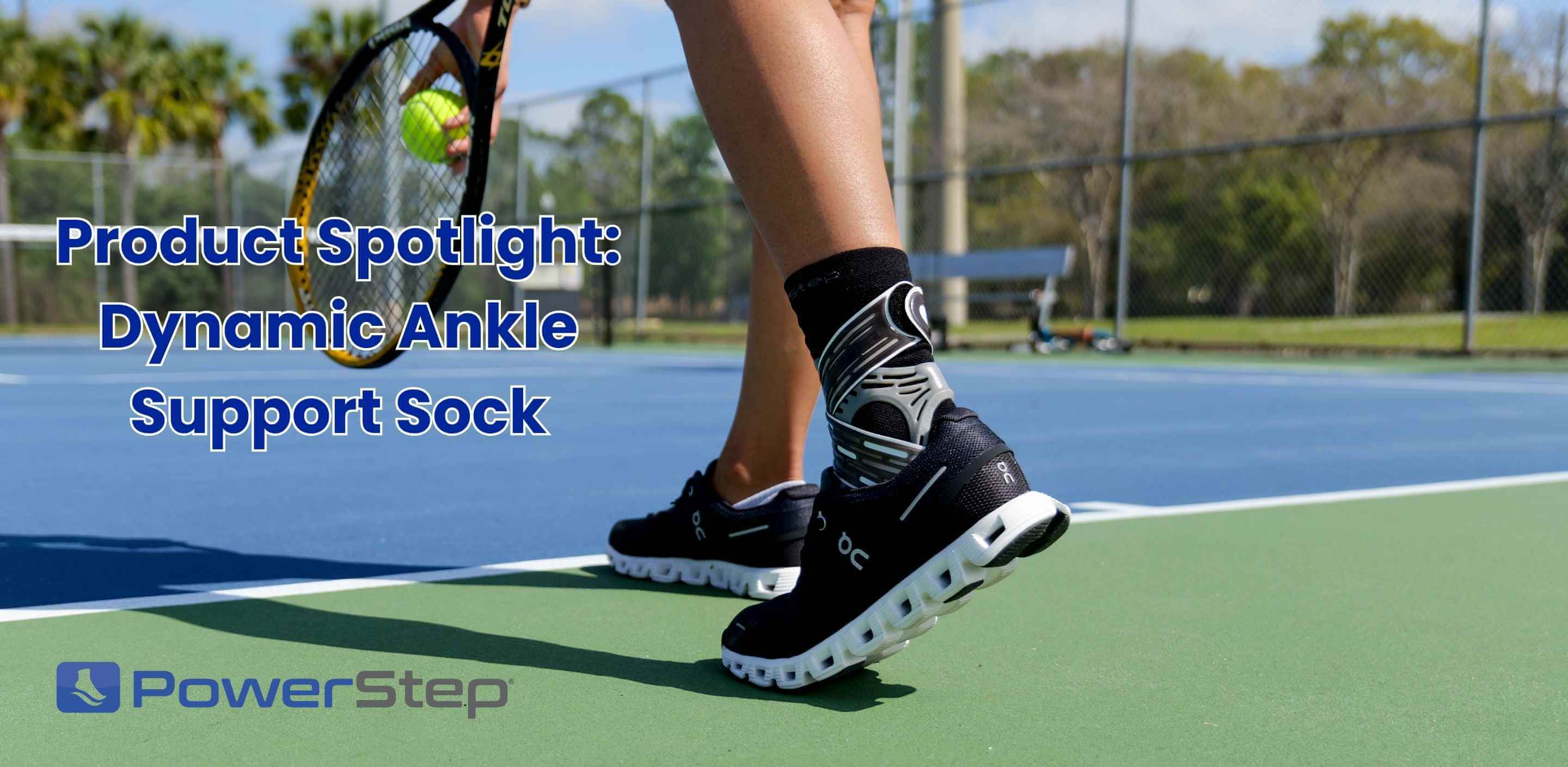 Person standing at the serve line of a tennis court, wearing the Dynamic Ankle Support Sock