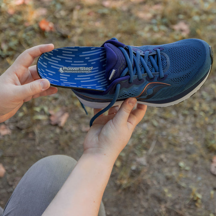 Woman placing PowerStep Morton’s Extension Insoles into navy blue tennis shoe.