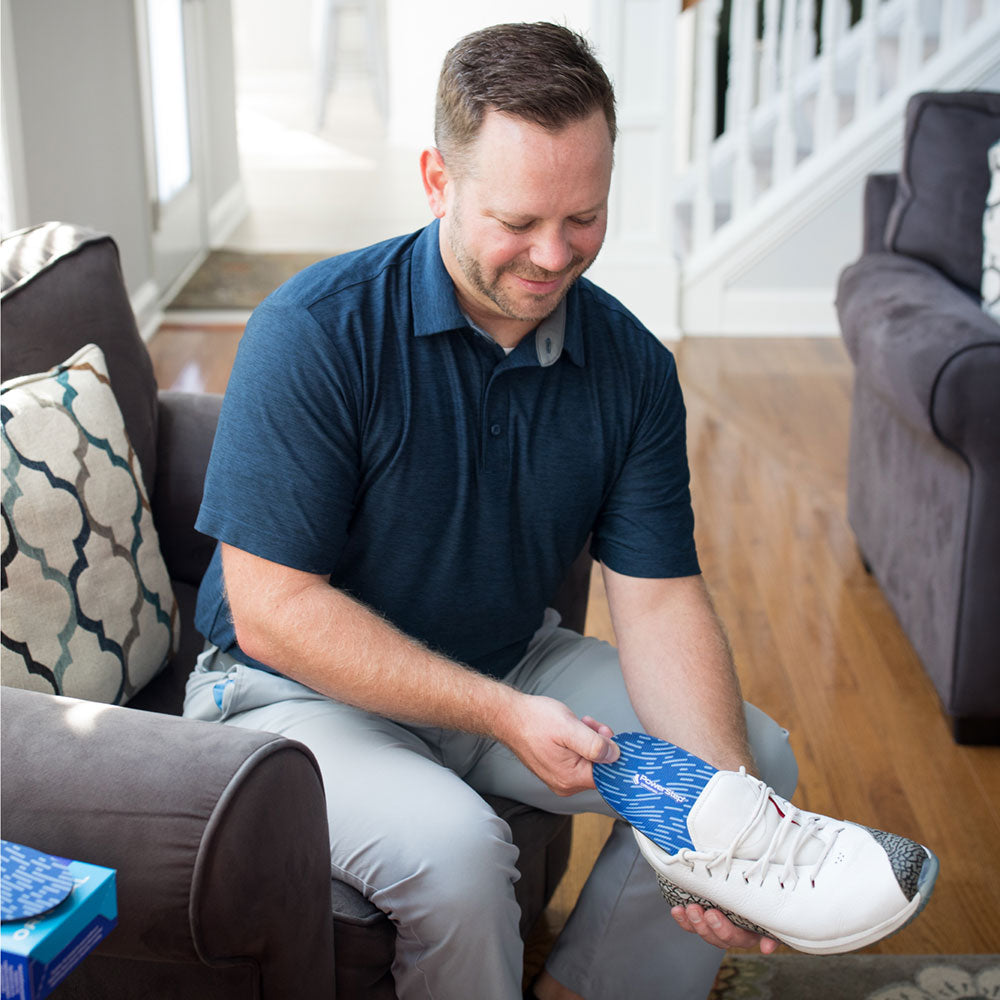 Man sitting on sofa in living room while putting PowerStep Original insoles into white sneakers