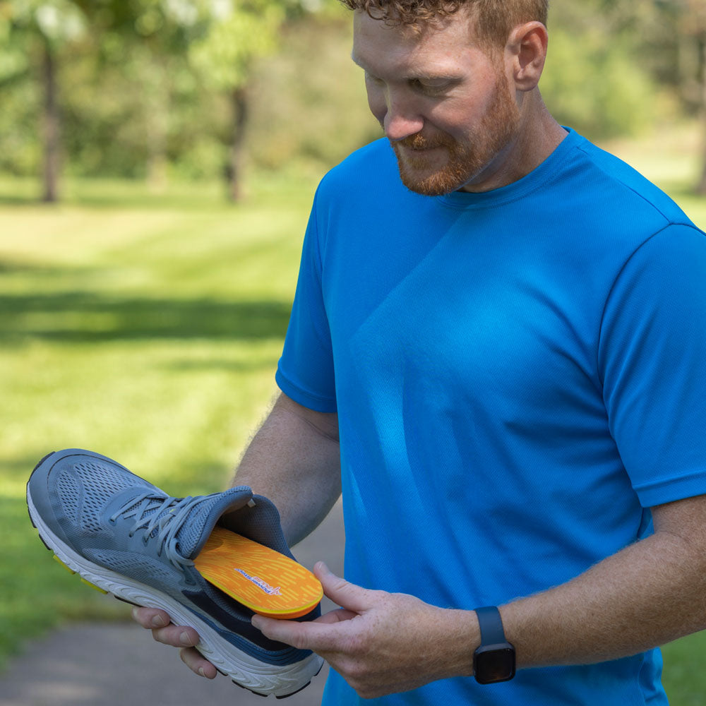 Man outside placing PULSE Performance insole into gray running shoe