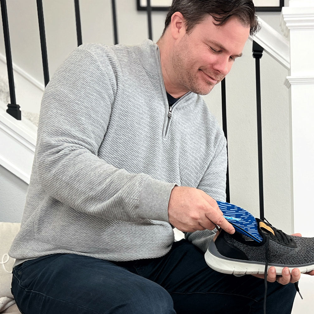 Man sitting on chair placing PowerStep Pinnacle insoles into dark gray sneakers