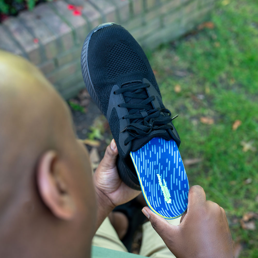 Man placing PowerStep Pinnacle Memory insole into black shoe.