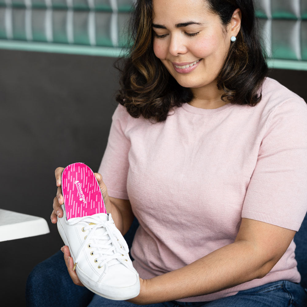 Woman sitting at table, placing PowerStep Pinnacle Pink into white canvas shoe.