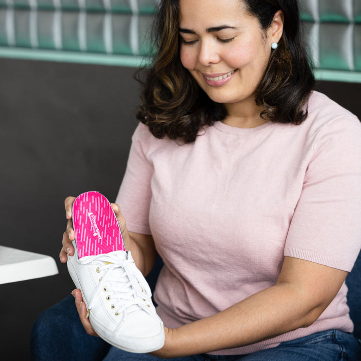 Woman sitting at table, placing PowerStep Pinnacle Pink into white canvas shoe.