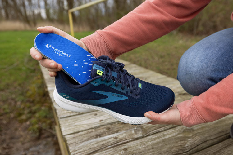 Person placing PowerStep bridge insoles into tennis shoes.