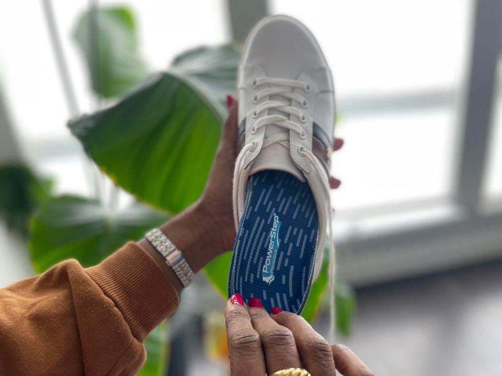 Woman placing PowerStep Pinnacle Insoles into white sneakers.