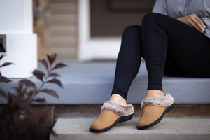 Woman sitting outside while wearing tan colored PowerStep Orthotic Slippers