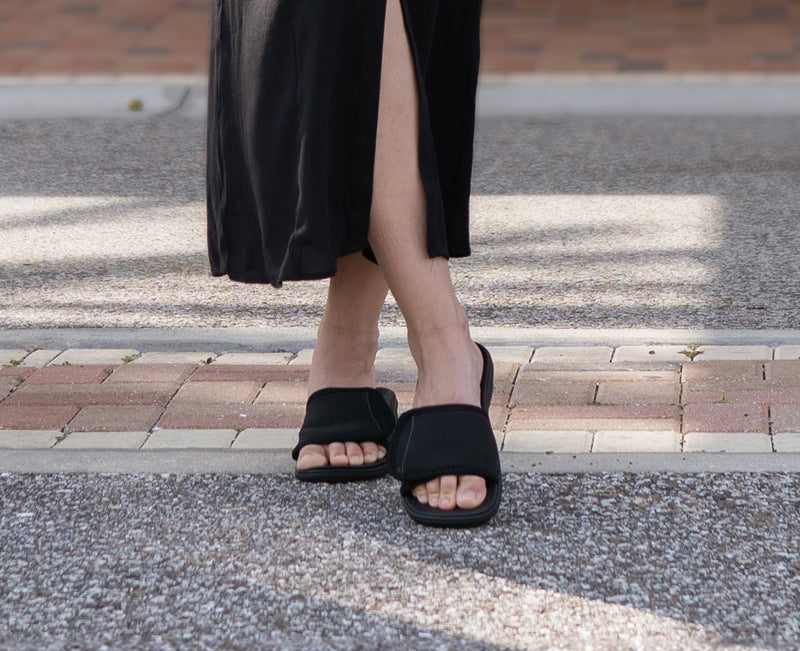 Woman standing outside of brick building, wearing PowerStep Slide orthotic sandals