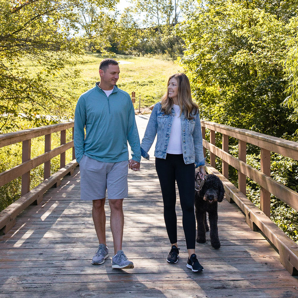 Husband and wife walking dog across wood bridge while wearing PowerStep insoles