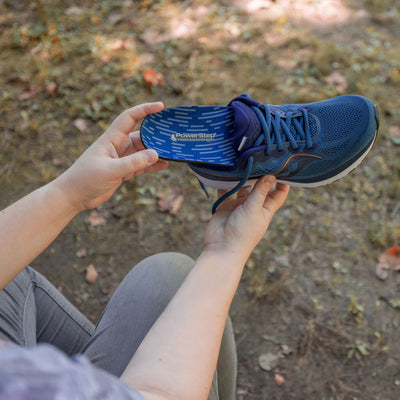 Woman placing PowerStep Morton's Extension insole into blue sneaker.