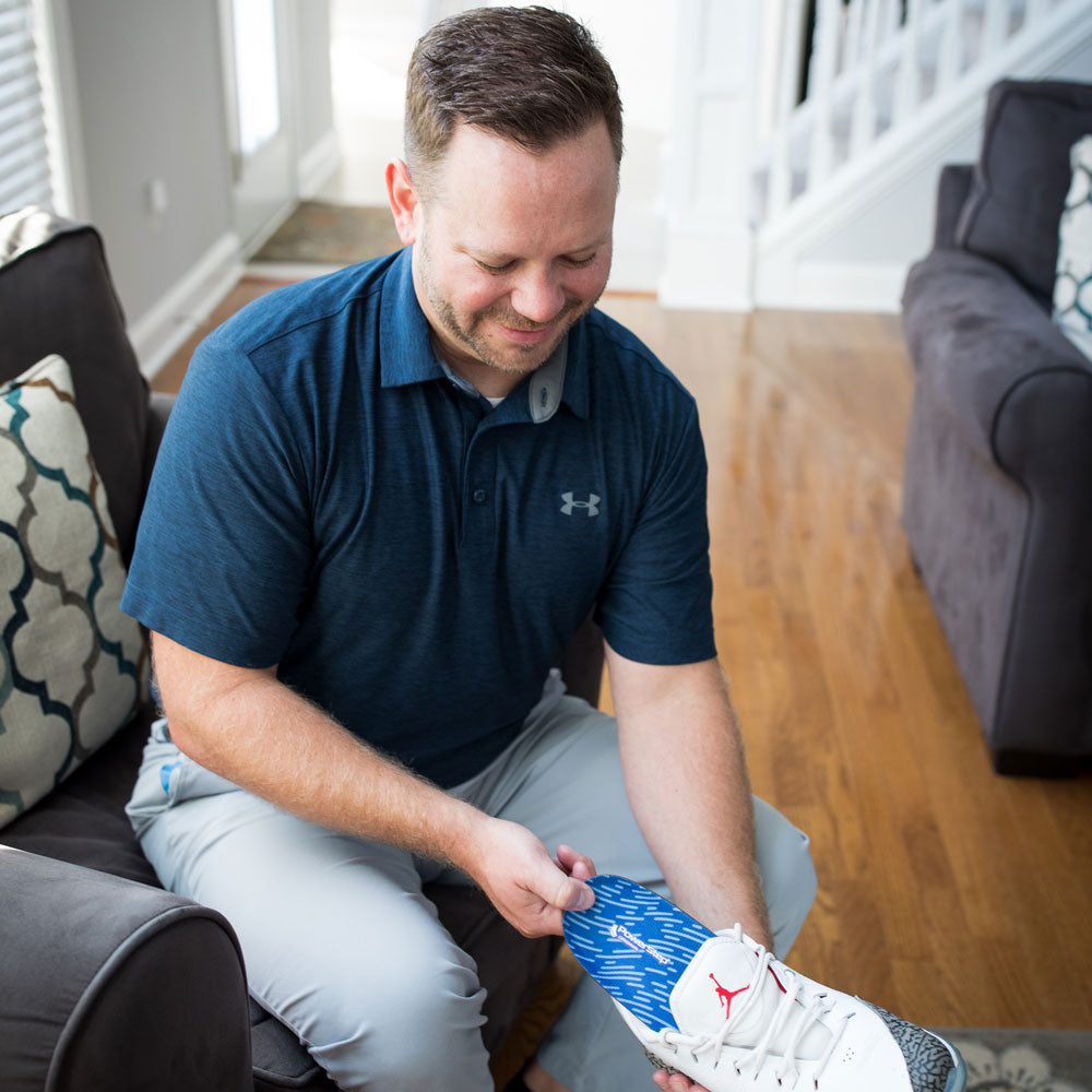 Man sitting on sofa in living room while putting PowerStep Original insoles into white sneakers