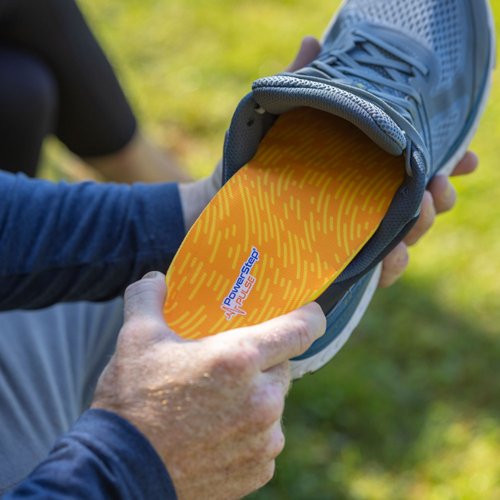 Man placing PowerStep PULSE Performance insoles into gray running shoe