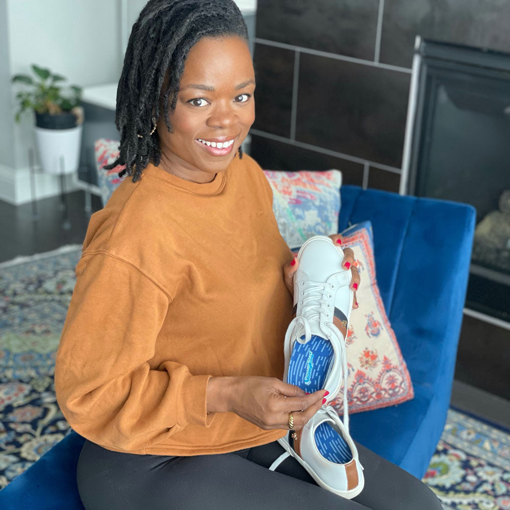 Woman sitting in living room showing white shoes with PowerStep Pinnacle insoles inside