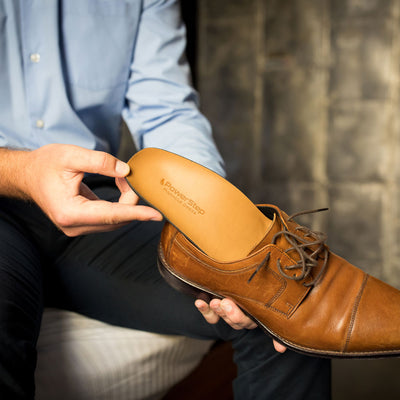 Person placing PowerStep Pinnacle Dress insoles into brown leather dress shoe