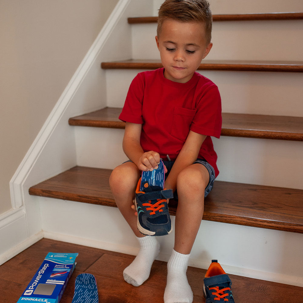 Little boy sitting on wood stairs while placing Pinnacle Junior insoles into dark blue and orange sneakers