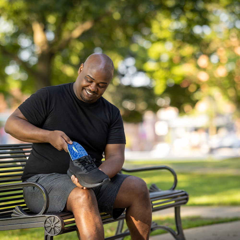 Man sitting on park bench while placing PowerStep Pinnacle Memory Foam insoles into black tennis shoes