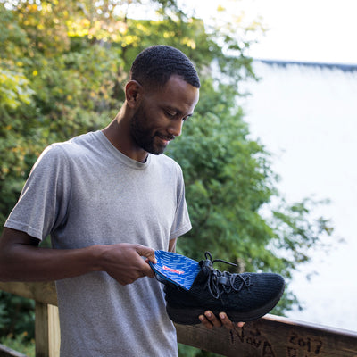 Man standing outside in front of green tree while holding up black tennis shoe and placing PowerStep Pinnacle Plus insoles inside