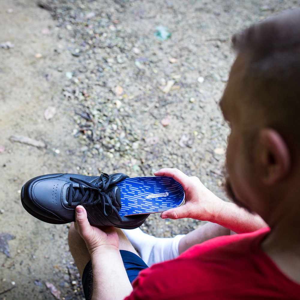 Over-the-shoulder view of man placing PowerStep Pinnacle Wide insoles into black shoe