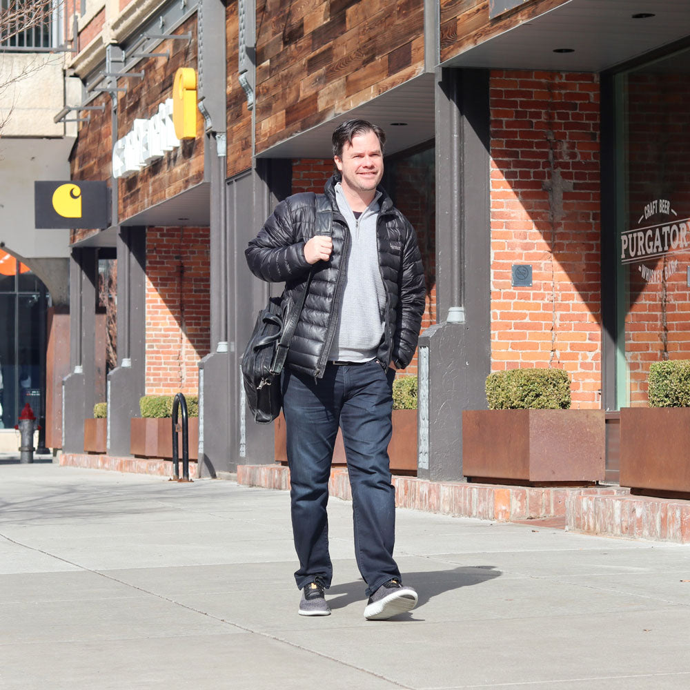 Man walking down sidewalk near brick buildings on a sunny winter day while wearing black winter coat and gray shoes with PowerStep Pinnacle Wool insoles inside to keep his feet warm