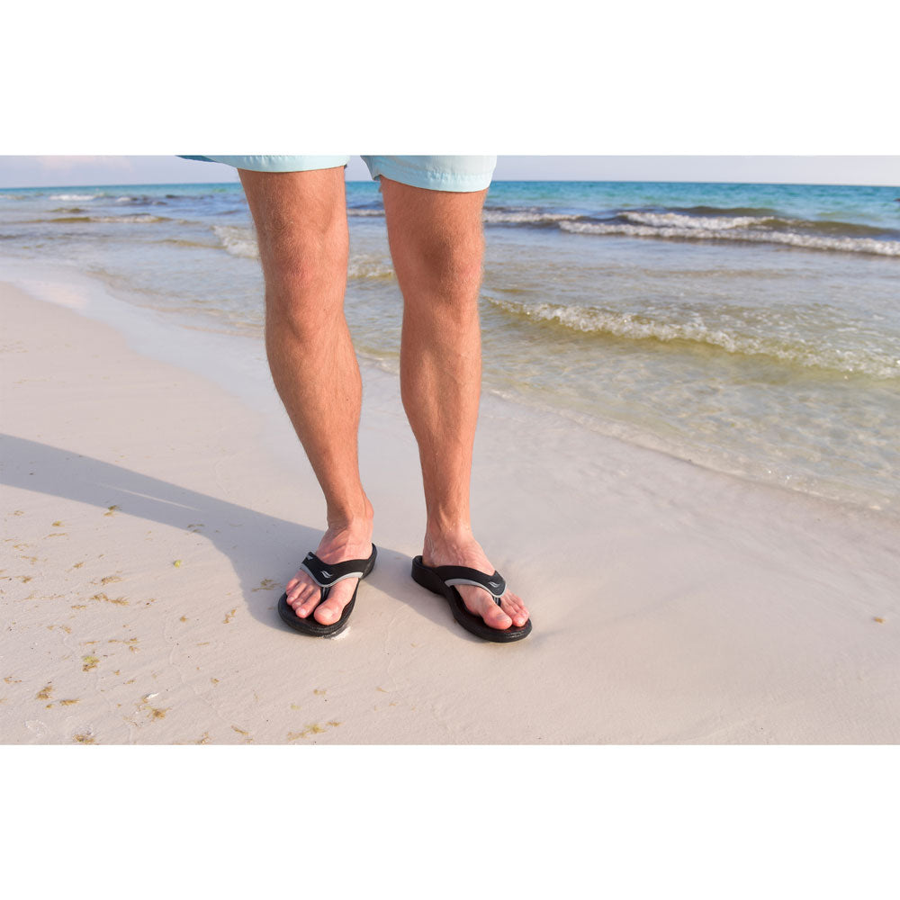 PowerStep Orthotic Arch Supporting Sandals for Men, men standing on beach in black and gray sandals with ocean waves in background #color_black-gray