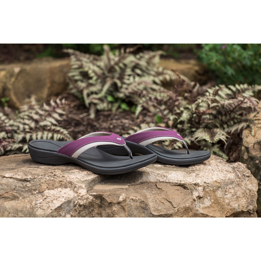 PowerStep Orthotic Arch Supporting Sandals for Women, plum and charcoal sandals with arch support sitting on rock with spring plants in the background #color_plum-charcoal