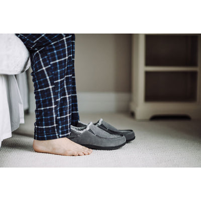 PowerStep Orthotic Arch Supporting slippers for Men, man stepping out of bed while wearing pajamas with arch supporting slippers sitting in front of his feet #color_charcoal-light-gray